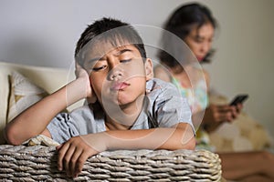 Young sad and bored Asian child at home couch feeling frustrated and unattended while mother networking on mobile phone as