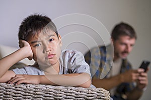 Young sad and bored child at home couch feeling frustrated and unattended while mother networking on mobile phone as internet