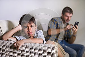 Young sad and bored child at home couch feeling frustrated and unattended while mother networking on mobile phone as internet