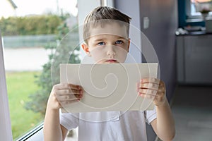 Young sad boy in a polo shirt, holding an empty copyspace sheet of paper