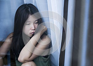 Young sad and depressed Asian Chinese woman looking thoughtful through window glass suffering pain and depression in sadness conce