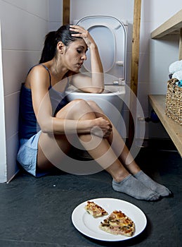 Young sad and depressed bulimic woman feeling sick guilty after vomiting pizza in WC toilet