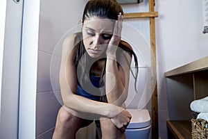 Young sad and depressed bulimic woman feeling sick sitting in toilet WC looking desperate and ill