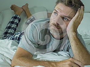 Young sad and depressed man lying thoughtful and pensive on bed looking away feeling lost thinking suffering some problem in