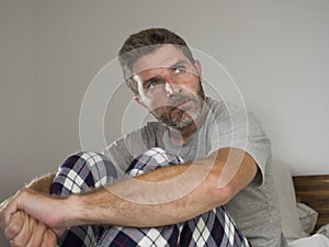 Young sad and depressed man lying thoughtful and pensive on bed looking away feeling lost thinking suffering some problem in