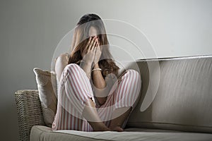 Young sad and depressed woman in pajamas at at home couch crying desperate feeling frustrated and upset suffering stress and