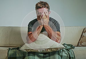 Young sad and desperate man at home sitting at sofa couch covering face with hands crying suffering depression and stress feeling