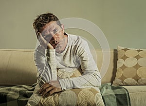 Young sad and desperate man at home sitting at sofa couch holding pillow suffering depression and stress feeling miserable looking