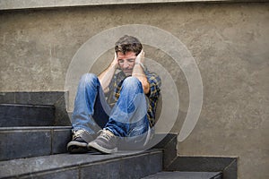 Young sad and desperate man sitting outdoors at street stairs suffering anxiety and depression feeling miserable crying in