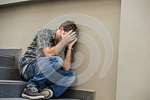 Young sad and desperate man sitting outdoors at street stairs suffering anxiety and depression feeling miserable crying in