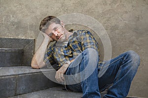 Young sad and desperate man sitting outdoors at street stairs suffering anxiety and depression feeling miserable crying in