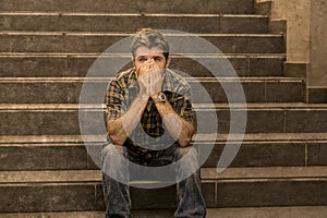 Young sad and desperate man sitting outdoors at street stairs suffering anxiety and depression feeling miserable crying in