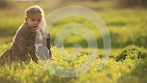Young sad girl lonely in grass field. A young girl is sitting picking grass alone in a grass field, frustrated or sad
