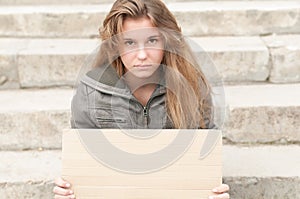 Young sad girl outdoor with blank cardboard sign.