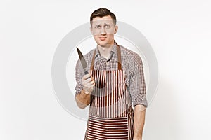 Young sad irritated dissatisfied man chef or waiter in striped brown apron, shirt holding sharp knife isolated on white