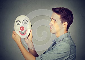 Young sad man with happy clown mask. Human emotions