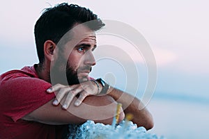 Young sad man by the sea looking at water