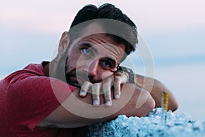 Young sad man by the sea looking at water