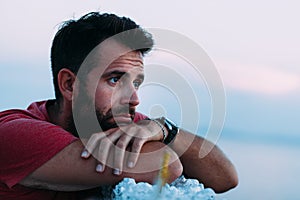 Young sad man by the sea looking at water