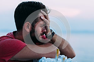 Young sad man by the sea looking at water