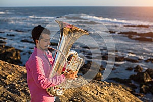 Young sad musician playing the trumpet on the ocean coast.