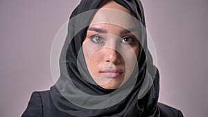 Young sad muslim girl in hijab is watching down and at camera, grey background, religious concept