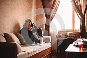 Young sad stressed woman using smart phone while sitting on sofa