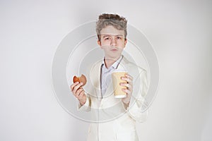 Young sad student guy in a business suit stands with a Cup of coffee and cookies in his hands on a white background in the Studio