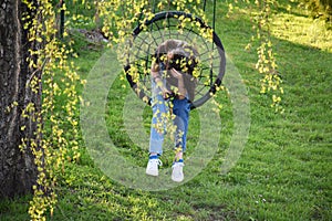 Young sad teen girl texting phone and resting in nest swing outdoors in summer day.