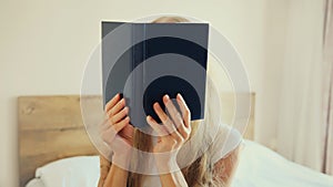 Young sad tired woman student with open book lying on the bed at home