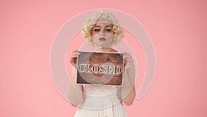 Young sad woman holding a brown sign with the inscription Closed. Young woman looking like Marilyn Monroe in studio on