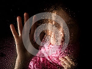 Young sad woman portrait behind the window in the rain with rain drops on it