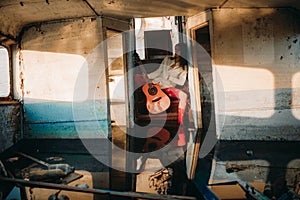 A young sad woman sits with guitar inside of old abandoned ship