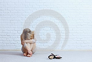 Young sad woman sitting on the floor near brick wall.