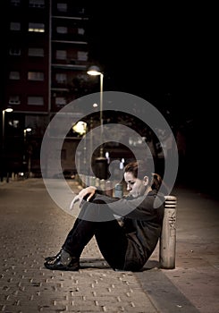 Young sad woman sitting on street ground at night alone desperate suffering depression left abandoned