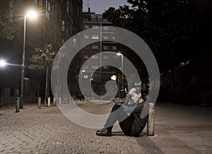 Young sad woman sitting on street ground at night alone desperate