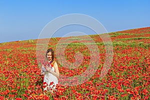 Young sad woman in white dress collects bouquet on poppy field