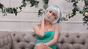 Young sad woman in wig have a painful feelings in neck at home
