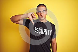 Young safeguard man with security t-shirt over yellow isolated background with angry face, negative sign showing dislike with
