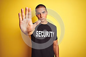Young safeguard man with security t-shirt over yellow isolated background with open hand doing stop sign with serious and