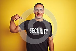 Young safeguard man with security t-shirt over yellow isolated background with surprise face pointing finger to himself