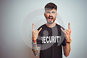 Young safeguard man with tattoo wering security uniform over isolated white background shouting with crazy expression doing rock