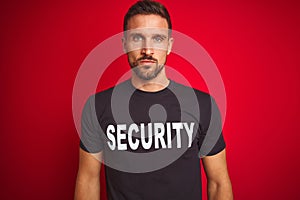 Young safeguard man wearing security uniform over red isolated background with serious expression on face