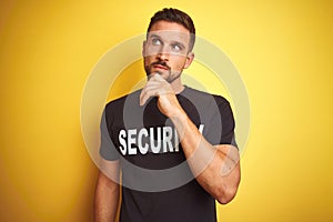 Young safeguard man wearing security uniform over yellow isolated background with hand on chin thinking about question, pensive