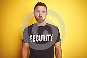 Young safeguard man wearing security uniform over yellow isolated background puffing cheeks with funny face