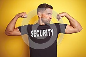 Young safeguard man wearing security uniform over yellow isolated background showing arms muscles smiling proud