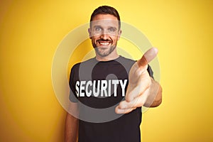 Young safeguard man wearing security uniform over yellow isolated background smiling friendly offering handshake as greeting and