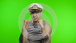 Young sailor man is angry and shows fists. Seaman guy in sailor`s vest