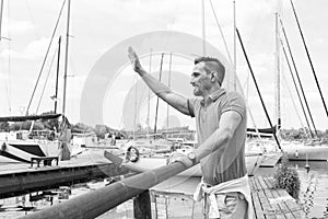 Young sailor waving up on pier with big smile. Yachtsman gives the command by hand to moor in dock. Man welcomes new boat in