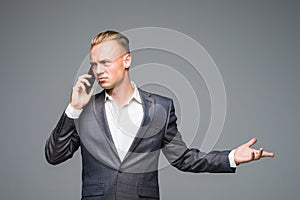 Young sales business person in elegant suit standing in front of clear empty grey wall background while talking on the phone with